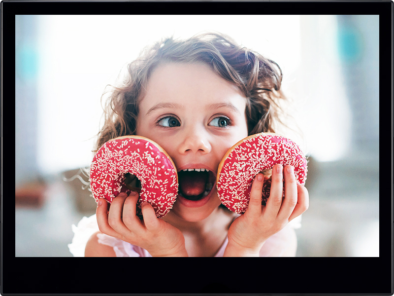 A small girl with doughnuts at home, looking at camera.