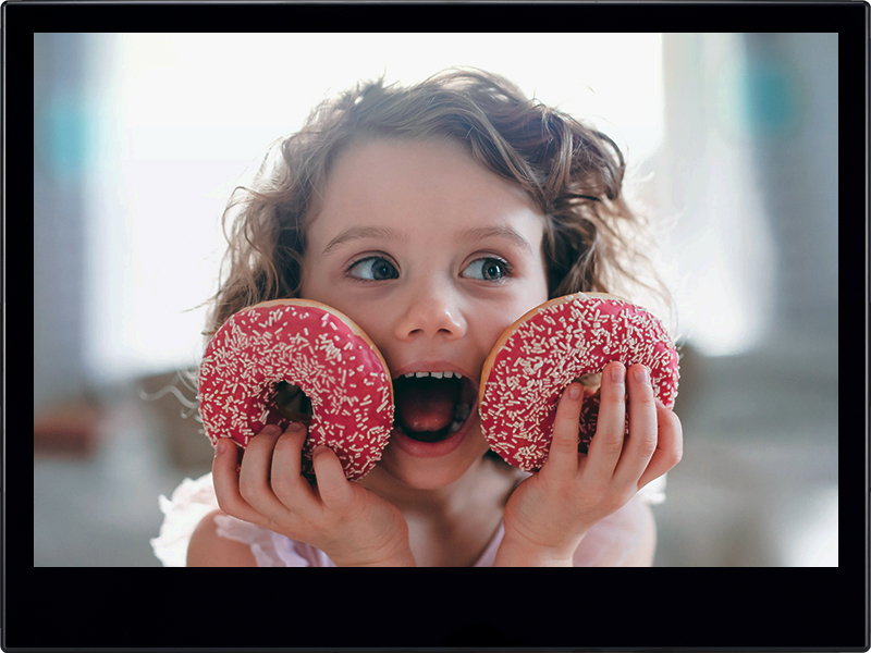 A small girl with doughnuts at home, looking at camera.
